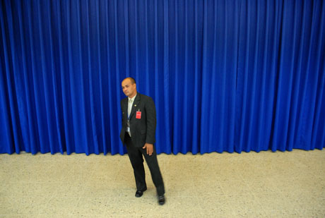 Un guardaespaldas de la presidencia cuida el lugar donde sería develado el cuadro en homenaje a Monseñor Romero, bajo un telón azul. Foto Mauro Arias