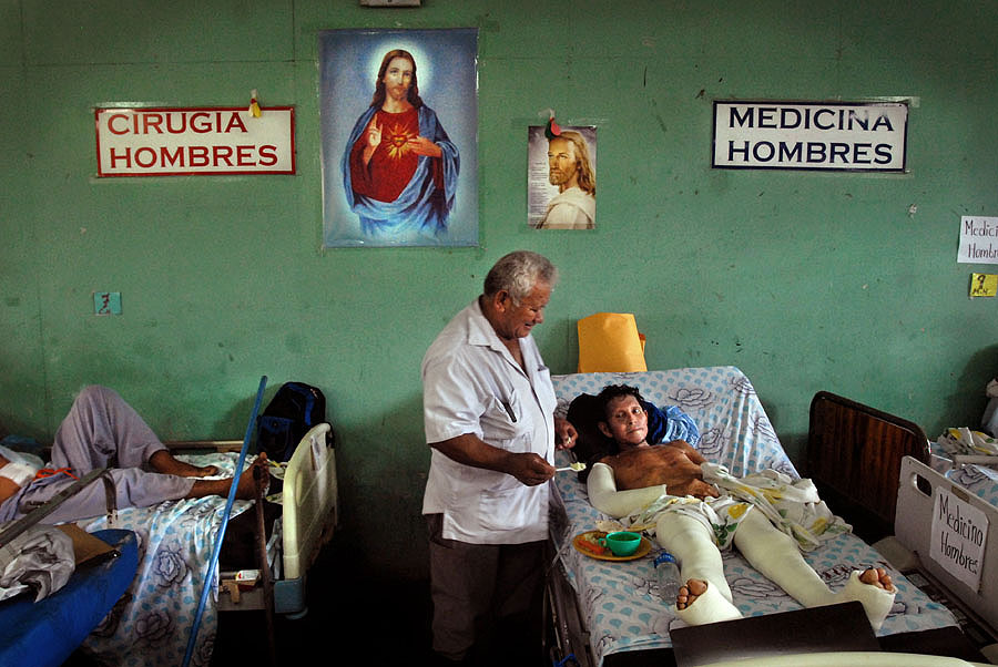 Medardo Romero, auxiliar de mantenimiento, deja su escoba de lado para dar de comer a Miguel Zepeda, paciente manco y cuyo único brazo está enyesado. Estas dos áreas, “cirugía hombres” y “medicina hombres” deberían estar separadas, pues los recién salidos del quirófano requieren el ambiente más pulcro posible para recuperarse.