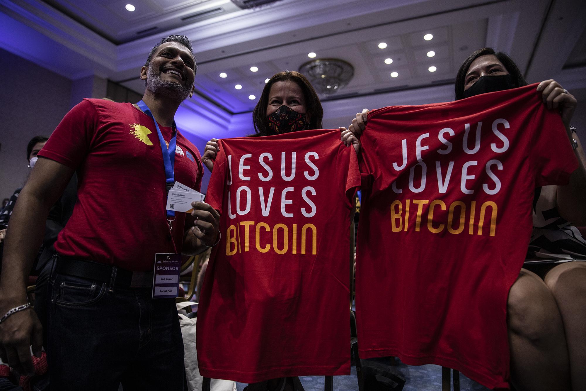 La Ministra de Economía, María Luisa Hayem, y la Ministra de Turismo, Morena Valdez, posan con una camisa con la leyenda, ''Jesús ama el Bitcoin'', junto Kurt Kumar de Rocket Fuel durante la convención Adopting Bitcoin A Lightning Summit El Salvador 2021. Foto de El Faro: Carlos Barrera