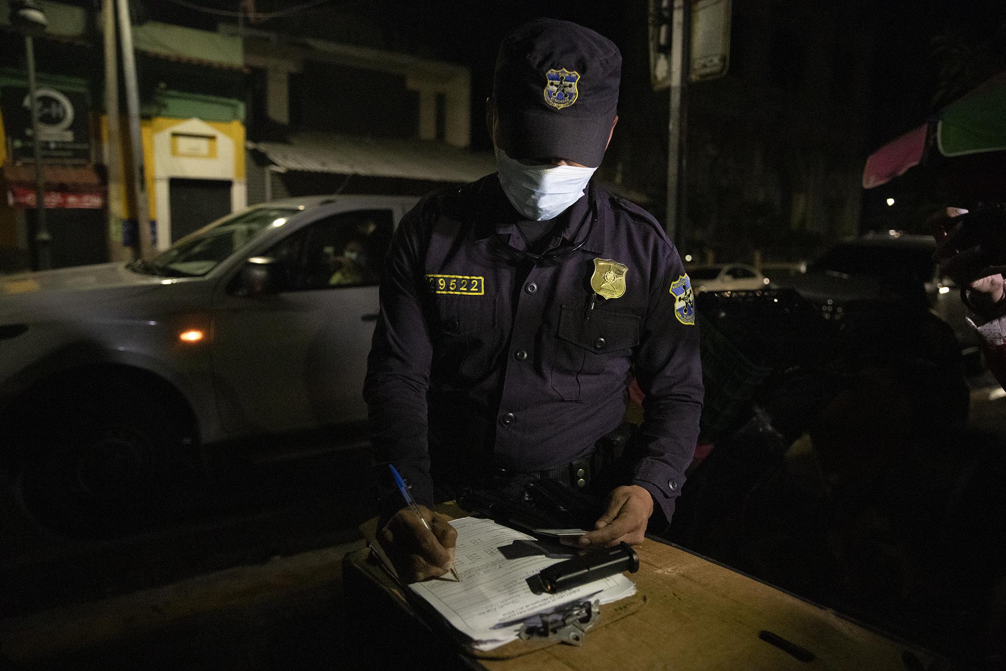 An agent with the National Civil Police (PNC) inspects the firearm permits of prosecutors as they attempt to raid the offices of the Ministry of Health in 2020, during investigations into corrupt pandemic-related government purchases. Photo: Carlos Barrera/El Faro